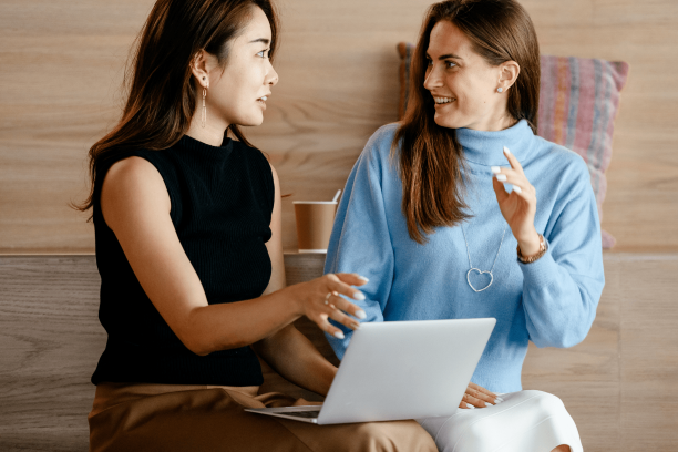 2 women talking while holding a laptop